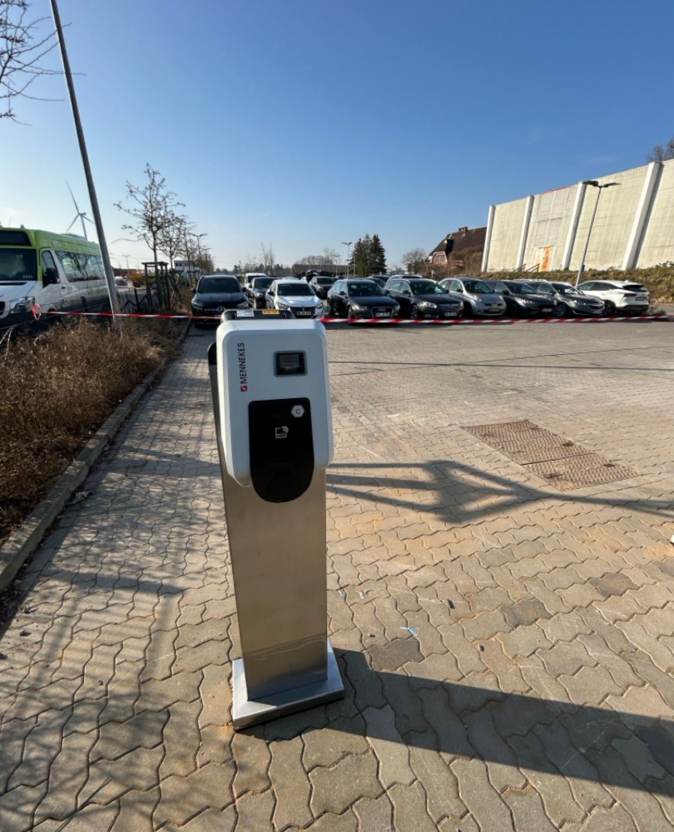 Freistehende E-Ladesäule (Stele) auf einem gepflasterten Firmenparkplatz bei blauem Himmel.